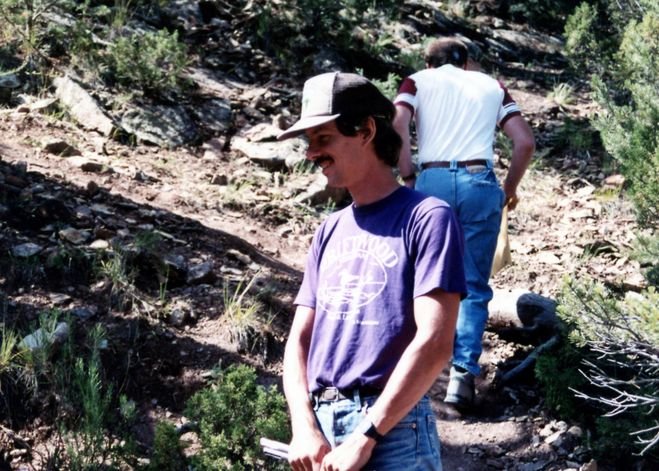 Color photo of Brian Small standing at the quarry site of a stegosaurus dinosaur. Circa 1992.
